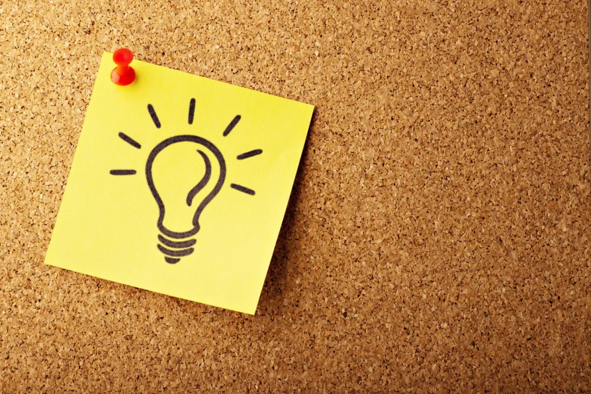 Yellow sticky note with a light bulb drawing pinned to a corkboard