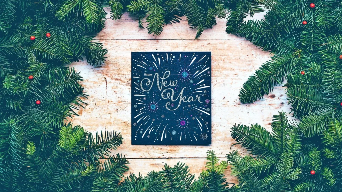 New Year card surrounded by evergreen branches on a wooden surface