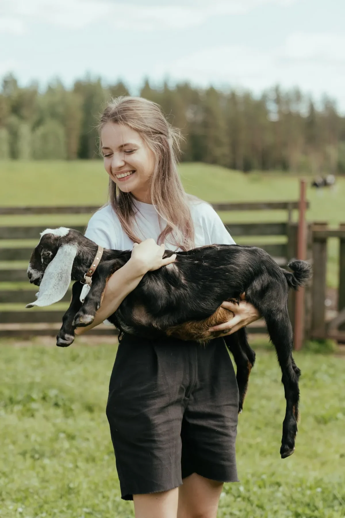 Woman holding a black goat in a pasture